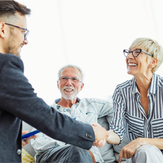 A financial professional shaking hands with a woman and her husband after securing indexed universal life insurance coverage for them.