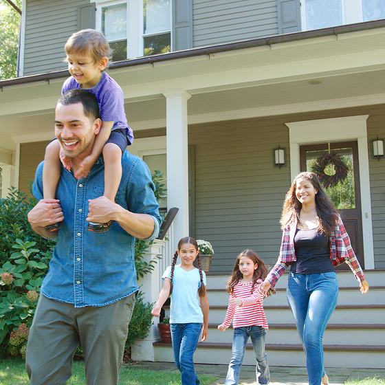 A smiling family of five walks out of their home.