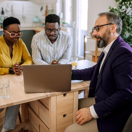 Three colleagues sit at a table reviewing a laptop.