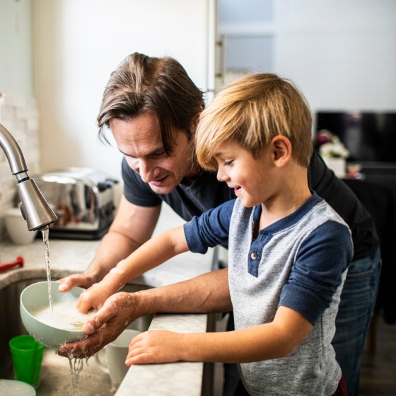 A father washing dishes with his son.