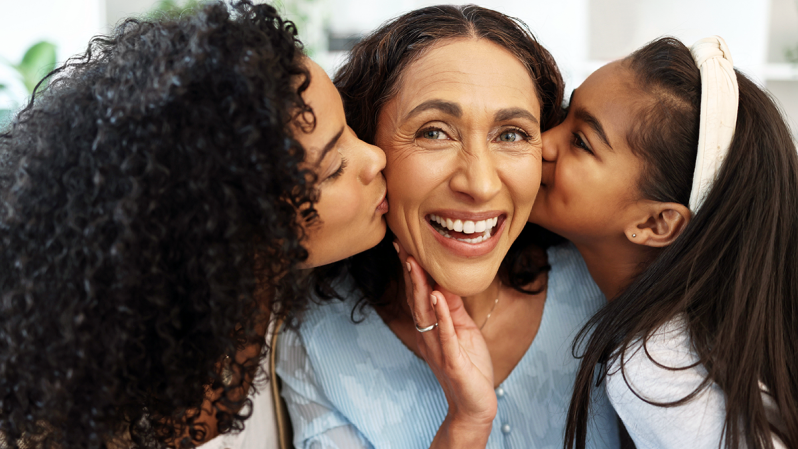 A mother being kissed on the cheeks by her daughters.
