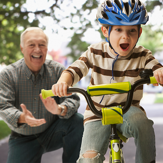 A grandfather teaching his grandson how to ride a bike.